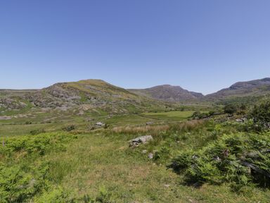 A grassy landscape with hills and scattered rocks under a clear blue sky at Llethr - Shepherds Hut in Llanbedr