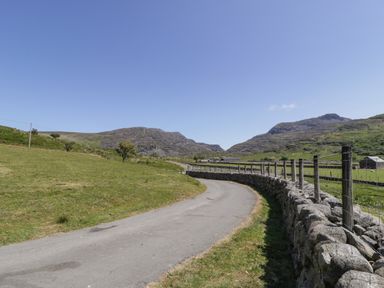 A country road with a stone wall and fence alongside green fields and hills in the background at Llethr - Shepherds Hut in Llanbedr