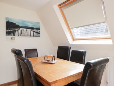 A wooden dining table with six black leather chairs in a room with a slanted ceiling at Owl Lodge in South Laggan near Invergarry