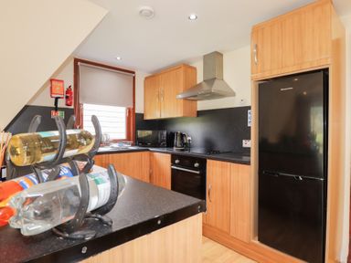 A kitchen with wooden cabinets black countertop black refrigerator and a wine rack at Owl Lodge South Laggan near Invergarry