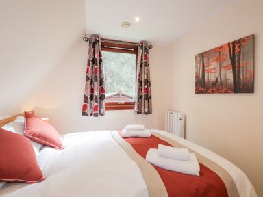 A bedroom with a double bed two red pillows folded towels on the bed a window with curtains and a forest painting on the wall at Owl Lodge South Laggan near Invergarry