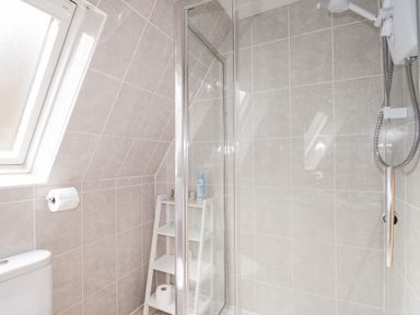 A bathroom with a shower, toilet, shelving unit with toiletries, and a window at Owl Lodge South Laggan near Invergarry
