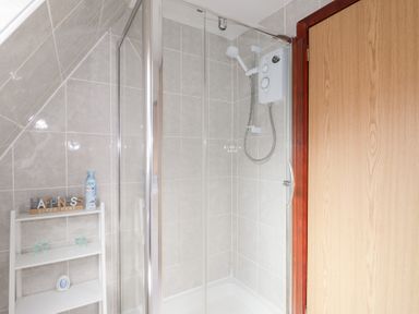A bathroom corner with a glass shower enclosure and a white shelving unit with toiletries at Owl Lodge South Laggan near Invergarry