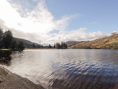 A lake with trees on the shore and hills in the background at Owl Lodge South Laggan near Invergarry