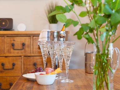 A wooden table with four champagne glasses grapes snacks and a vase with green leaves at 7 Four Seasons in Carbis Bay