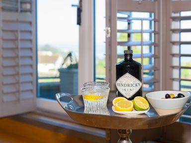 A bottle of Hendrick's gin with two glasses lemon slices and a bowl of olives on a tray in a room with window shutters at 7 Four Seasons in Carbis Bay