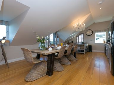 A kitchen dining area with a wooden table and wicker chairs a chandelier and windows at 7 Four Seasons in Carbis Bay