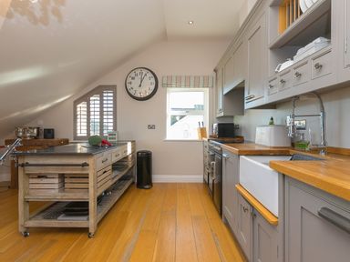 A kitchen with wooden floors grey cabinets a central island and a large wall clock at 7 Four Seasons in Carbis Bay