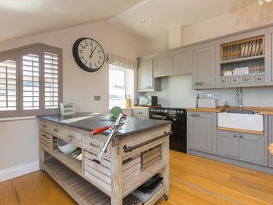 A kitchen with a wooden island table and gray cabinets with a black stove and a farmhouse sink at 7 Four Seasons in Carbis Bay