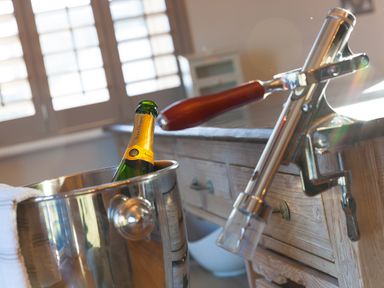 A bottle of Veuve Clicquot champagne in an ice bucket with a wooden handled corkscrew attached to a wooden counter at 7 Four Seasons in Carbis Bay