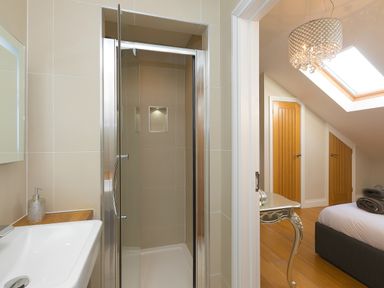 A bathroom with a shower and a sink next to a bedroom with a bed a skylight and wooden doors at 7 Four Seasons in Carbis Bay