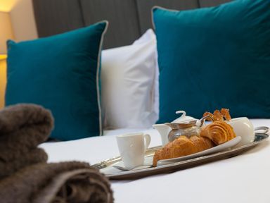 A tray with croissants, a cup, a teapot, and sugar bowl on a bed with blue pillows at 7 Four Seasons in Carbis Bay