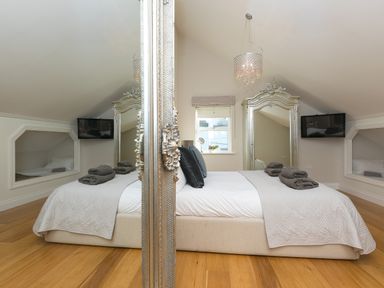 A bedroom with a bed folded towels on it two black cushions mirrors on each side and a window at 7 Four Seasons in Carbis Bay