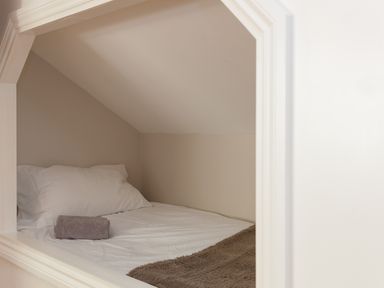 A small bed with white pillows a rolled towel and a brown blanket in a compact alcove at 7 Four Seasons in Carbis Bay