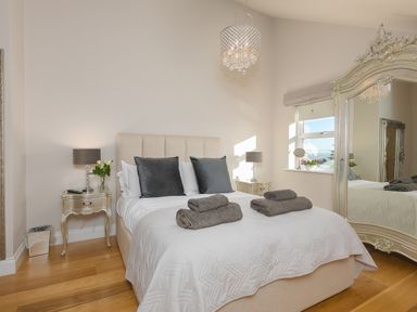 A bedroom with a bed with pillows and towels two bedside tables with lamps a large mirror and a window at 7 Four Seasons in Carbis Bay