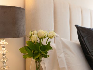 A vase with white roses next to a lamp and pillows on a bed at 7 Four Seasons in Carbis Bay