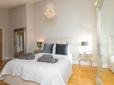 A bedroom with a bed with gray pillows and towels on it two bedside tables with lamps and a large mirror on the floor at 7 Four Seasons in Carbis Bay
