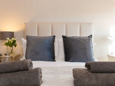 A bed with two grey pillows and folded towels with bedside tables and lamps at 7 Four Seasons in Carbis Bay