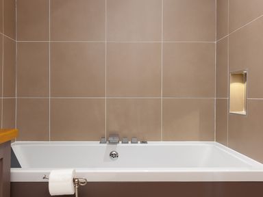 A bathtub with modern fixtures and a toilet paper holder in a tiled bathroom at 7 Four Seasons in Carbis Bay