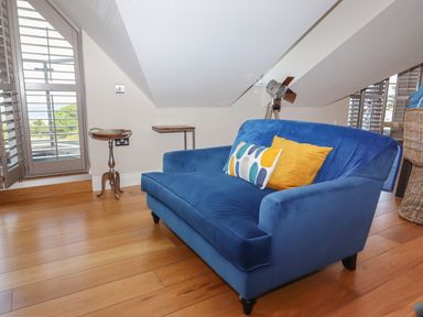 A blue sofa with two cushions near a window and small tables on wooden floor at 7 Four Seasons in Carbis Bay