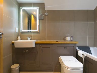 A bathroom with a sink, illuminated mirror, toilet, bathtub, and wooden countertop at 7 Four Seasons in Carbis Bay