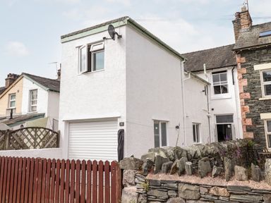 A white two-story house with a closed garage door a wooden fence and a stone wall at Dovestones in Keswick