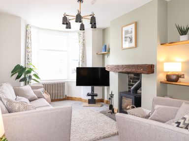 A living room with two sofas a TV a wood burning stove and a large window at Dovestones in Keswick