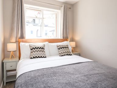 A bedroom with a double bed two patterned cushions bedside tables with lamps and a window with curtains at Dovestones in Keswick