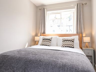 A bedroom with a double bed white pillows chevron patterned cushions bedside tables with lamps and windows with curtains at Dovestones in Keswick