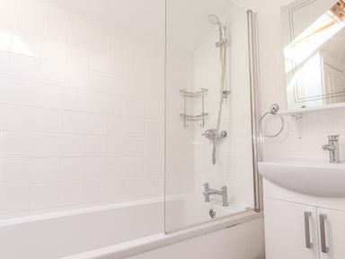 A bathroom with a bathtub shower combination a sink with cabinet under a mirror and a towel ring at Dovestones in Keswick