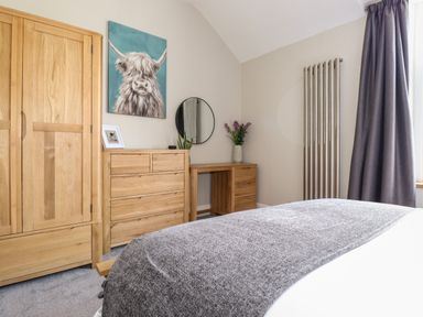 A bedroom with wooden wardrobe dresser desk a bed with gray throw and a window with gray curtains at Dovestones in Keswick