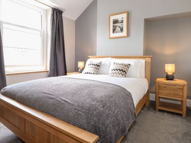 A bedroom with a wooden double bed grey blanket two bedside tables with lamps and a framed picture on the wall at Dovestones in Keswick