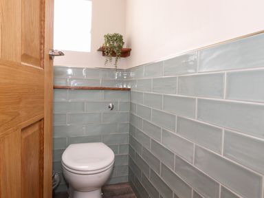 A small bathroom with a closed toilet and light blue tiled walls at Dovestones in Keswick