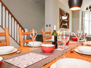 A dining table set with plates bowls wine glasses and a bottle of wine in a room with wooden chairs and stairs at Dovestones in Keswick
