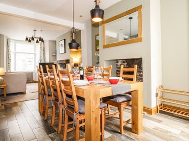 A dining area with a wooden table set for six with chairs and pendant lights at Dovestones in Keswick