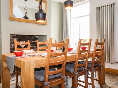 A dining area with a wooden table and six chairs set with plates bowls wine glasses and a bottle at Dovestones in Keswick