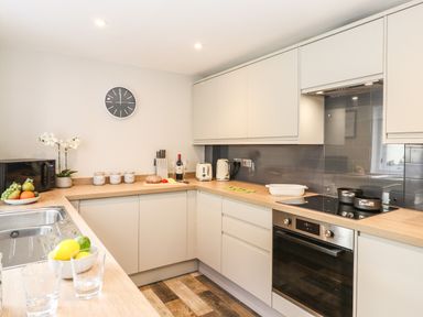 A kitchen with beige cabinets a microwave fruit bowls a sink a clock and cooking utensils at Dovestones in Keswick
