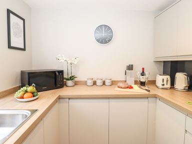 A kitchen countertop with a microwave fruit bowl kettle toaster bread wine and a clock on the wall at Dovestones in Keswick