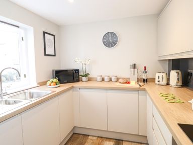 A kitchen with white cabinets wooden countertops a microwave a bowl of fruit and a clock on the wall at Dovestones in Keswick
