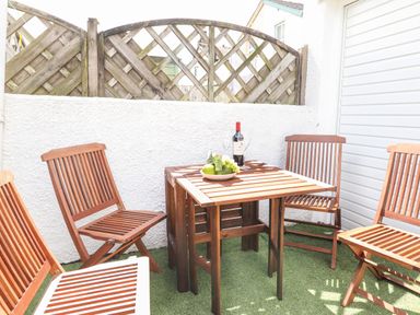 An outdoor seating area with a wooden table, four wooden chairs, a bottle of wine, two wine glasses, and a bowl of fruit at Dovestones in Keswick