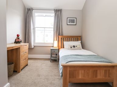 A bedroom with a single wooden bed a bedside table with a lamp a wooden desk with drawers and a window with curtains at Dovestones in Keswick