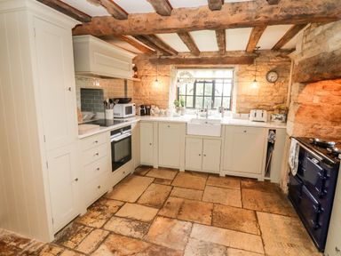 A kitchen with stone walls wooden beams white cabinets and tiled floor at The Small House Near Bourton-On-The-Water