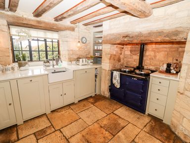A kitchen with a stone floor white cabinets a double basin sink and a dark blue stove at The Small House Near Bourton-On-The-Water