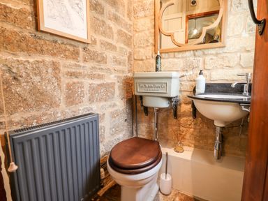 A small bathroom with a toilet a sink a mirror and a radiator on stone walls at The Small House Near Bourton-On-The-Water
