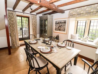 A dining room with wooden table set for six near windows and glass door at The Small House Near Bourton-On-The-Water
