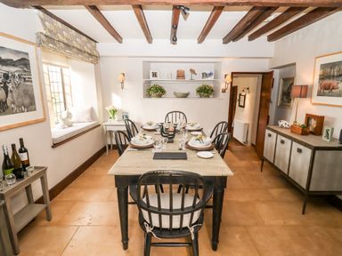 A dining room with a table set for six with black chairs and wooden beams on the ceiling at The Small House Near Bourton-On-The-Water