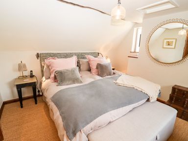 A bedroom with a bed with pink and gray pillows two bedside tables and a large round mirror at The Small House Near Bourton-On-The-Water