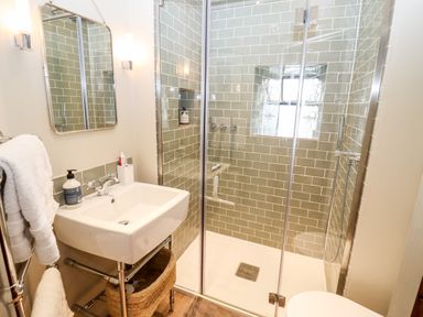 A bathroom with a sink a mirror and a glass shower enclosure with green tiled walls at The Small House Near Bourton-On-The-Water