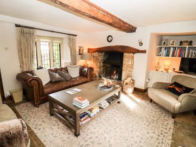 A living room with a brown leather sofa gray armchair coffee table and fireplace at The Small House Near Bourton-On-The-Water