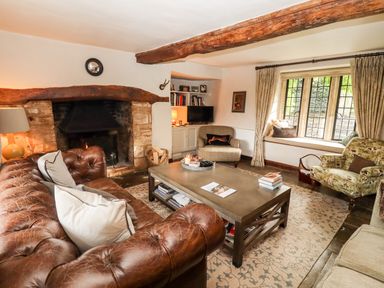 A living room with a leather sofa a stone fireplace wooden beams and a window seat at The Small House Near Bourton-On-The-Water